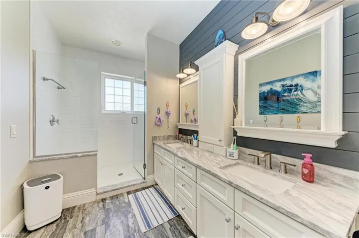 Full bath with baseboards, double vanity, a sink, and a stall shower
