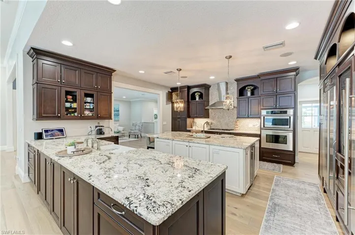 Kitchen with an island with sink, dark brown cabinetry, wall chimney exhaust hood, appliances with stainless steel finishes, and visible vents