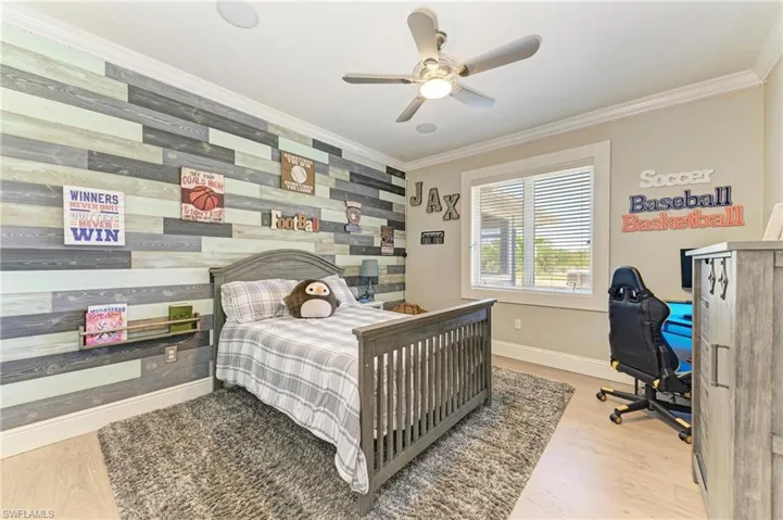 Bedroom with baseboards, wood finished floors, an accent wall, and crown molding