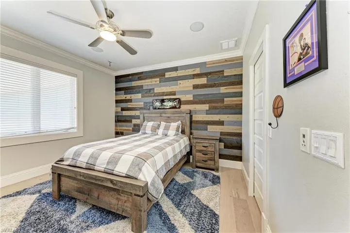 Bedroom with crown molding, an accent wall, wooden walls, light wood-type flooring, and visible vents