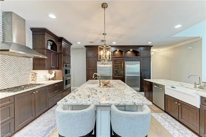 Kitchen featuring an inviting chandelier, stainless steel appliances, backsplash, a sink, and wall chimney range hood