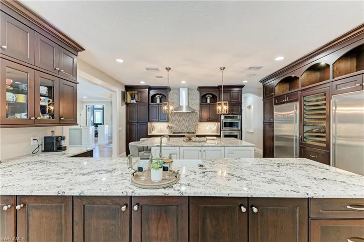 Kitchen featuring stainless steel built in fridge, wall chimney exhaust hood, dark brown cabinets, and open shelves