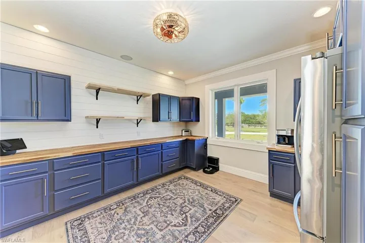 Kitchen featuring butcher block countertops, blue cabinets, freestanding refrigerator, and light wood finished floors