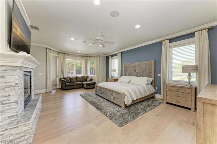 Bedroom featuring a fireplace, ornamental molding, visible vents, and light wood-style floors