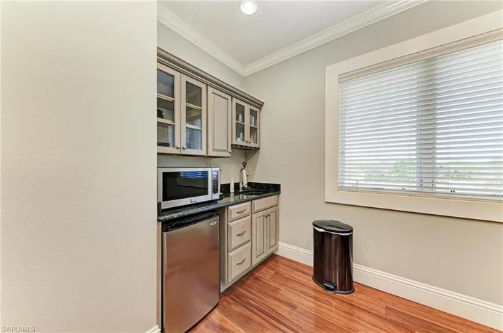 Kitchen with a sink, refrigerator, glass insert cabinets, stainless steel microwave, and ornamental molding