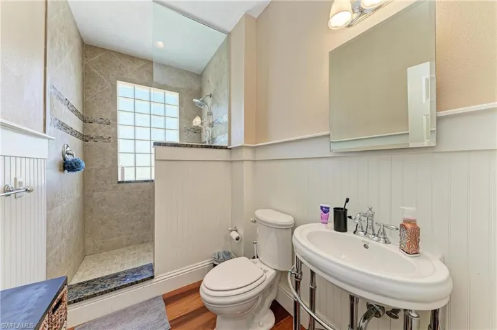 Full bathroom with a wainscoted wall, wood finished floors, toilet, a sink, and a walk in shower