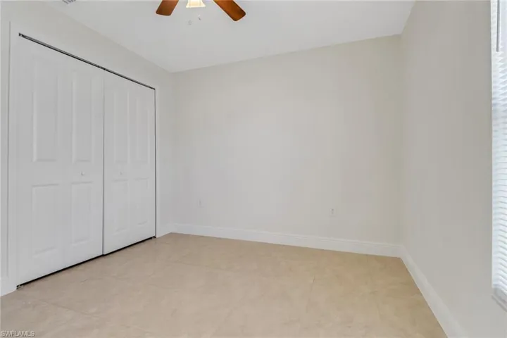 Unfurnished bedroom with a closet, light tile patterned flooring, baseboards, and a ceiling fan
