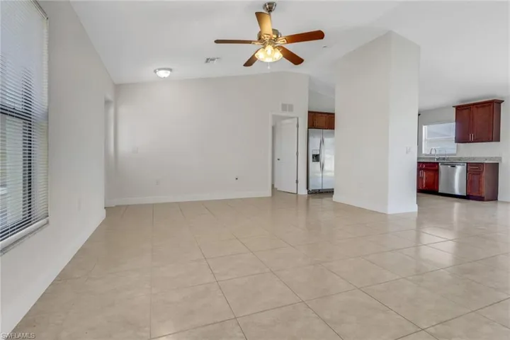 Unfurnished living room featuring lofted ceiling, baseboards, light tile patterned floors, visible vents, and ceiling fan