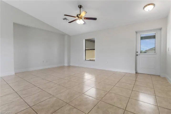 Empty room with baseboards, light tile patterned floors, a ceiling fan, visible vents, and lofted ceiling