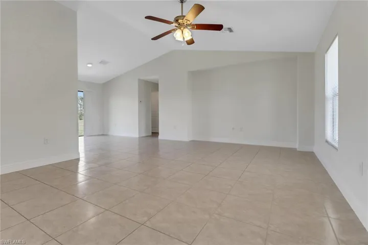 Empty room with visible vents, baseboards, ceiling fan, light tile patterned flooring, and lofted ceiling