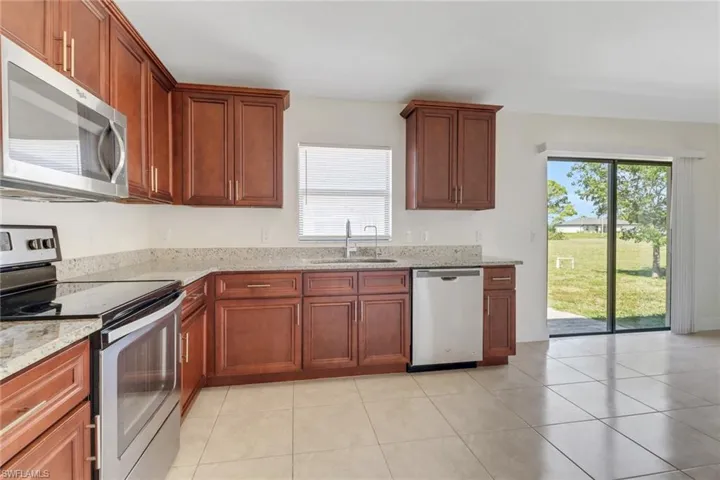 Kitchen with light tile patterned flooring, a sink, light stone countertops, and stainless steel appliances