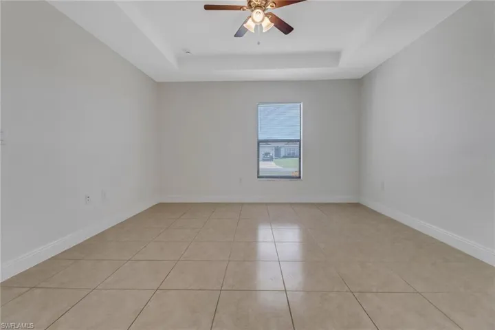 Empty room with baseboards, a tray ceiling, light tile patterned flooring, and ceiling fan