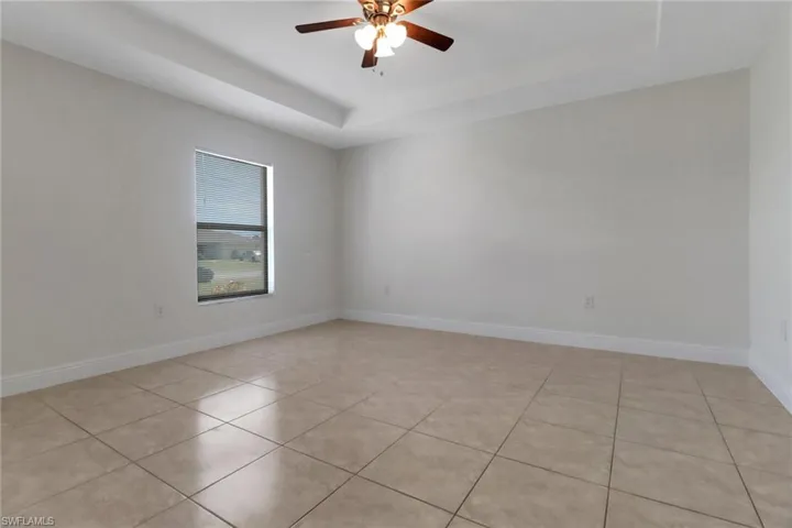 Spare room featuring ceiling fan, a tray ceiling, baseboards, and light tile patterned flooring
