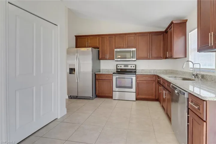 Kitchen with a sink, brown cabinetry, vaulted ceiling, stainless steel appliances, and light stone counters