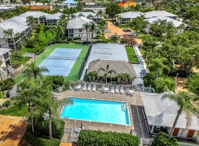 Outdoor swimming pool with surrounding lounge chairs, a covered tiki-style structure, and a tennis court