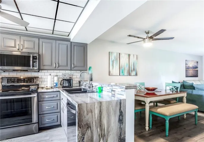 Kitchen featuring grey shaker-style cabinetry, stainless steel appliances, white subway tile backsplash, and a waterfall-edge countertop
