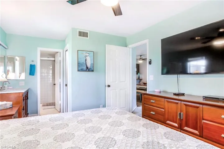 Light-colored walls featuring a ceiling fan, wood-finish dresser, and a large wall-mounted screen