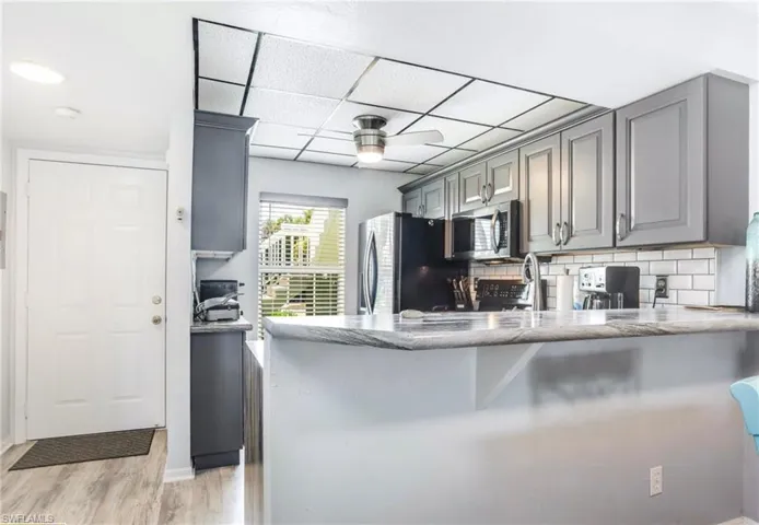 Kitchen featuring gray shaker-style cabinetry, a white subway tile backsplash, and a light-toned countertop with a breakfast bar