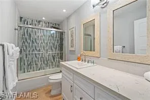 Bathroom with enclosed tub / shower combo, vanity, and light wood-style floors