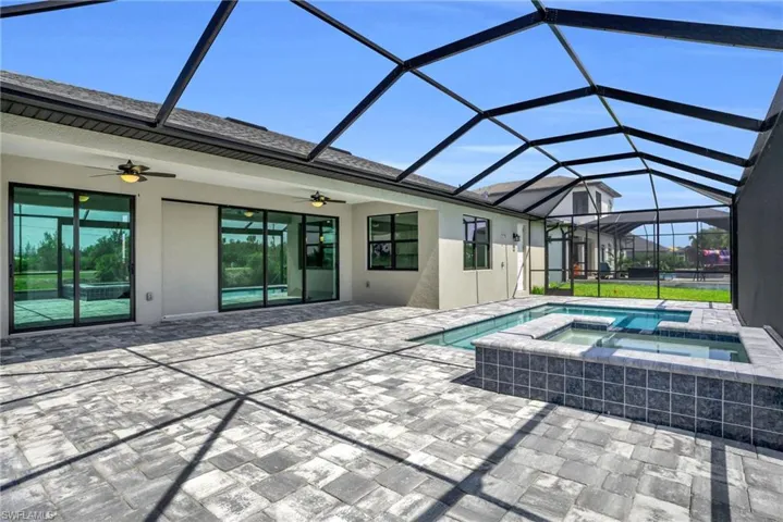 View of pool featuring ceiling fan, a patio, glass enclosure, and an in ground hot tub