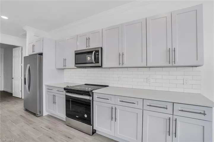 Kitchen with white cabinets, light hardwood / wood-style flooring, stainless steel appliances, crown molding, and decorative backsplash