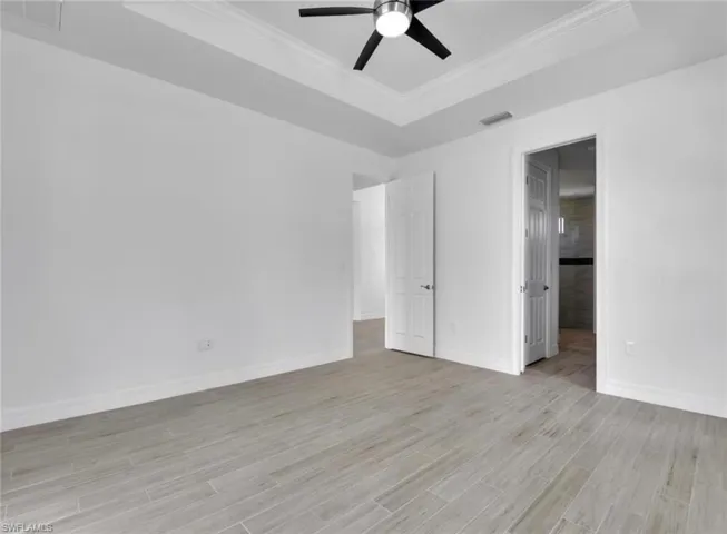 Unfurnished bedroom featuring a raised ceiling, light hardwood / wood-style floors, crown molding, and ceiling fan