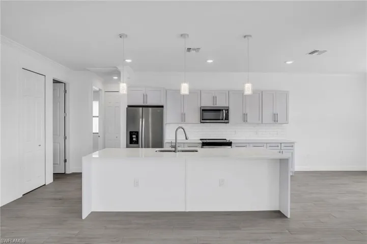 Kitchen featuring an island with sink, appliances with stainless steel finishes, hanging light fixtures, and sink