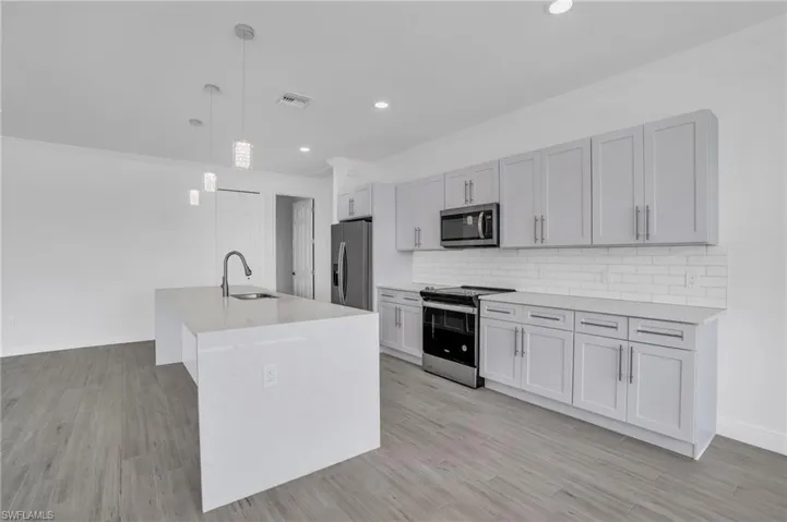 Kitchen featuring stainless steel appliances, an island with sink, light hardwood / wood-style floors, and decorative light fixtures