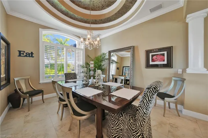 Tiled dining space featuring ornate columns, ornamental molding, a tray ceiling, and a chandelier