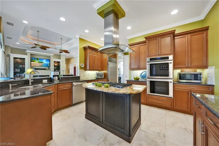 Kitchen featuring crown molding, island exhaust hood, appliances with stainless steel finishes, and dark stone counters