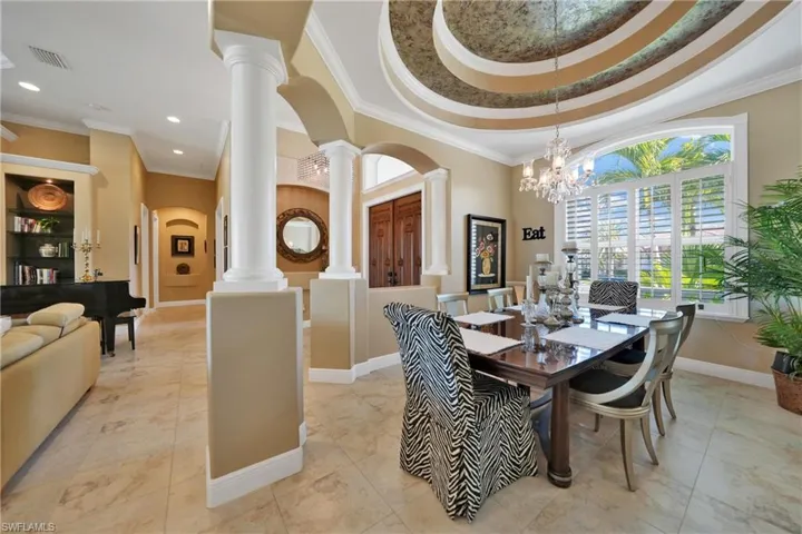 Dining room with a raised ceiling, decorative columns, crown molding, and a notable chandelier