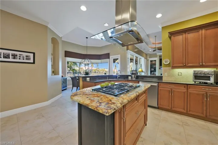 Kitchen with appliances with stainless steel finishes, dark stone counters, island range hood, sink, and a center island