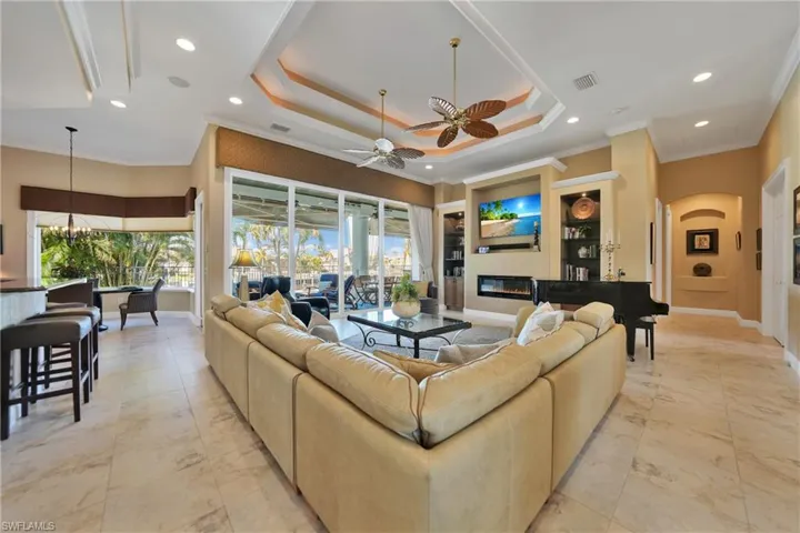 Living room with ceiling fan with notable chandelier, crown molding, and a tray ceiling