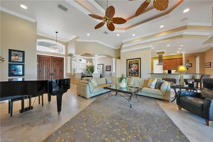 Living room with ceiling fan with notable chandelier, ornamental molding, a towering ceiling, and ornate columns