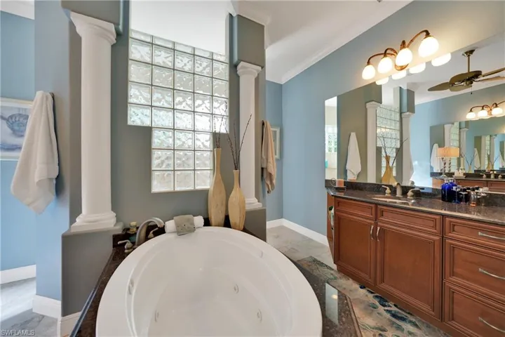 Bathroom featuring a tub to relax in, ornate columns, ceiling fan, and ornamental molding