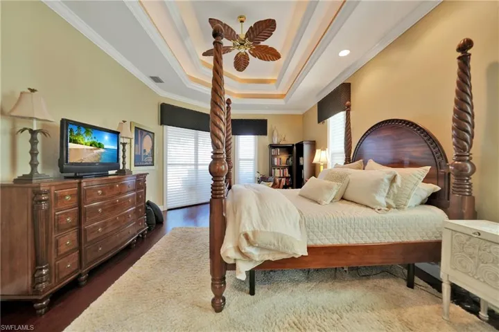 Bedroom featuring ceiling fan, a raised ceiling, ornamental molding, and dark wood-type flooring