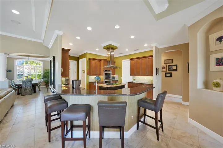 Kitchen featuring island exhaust hood, a kitchen bar, dark stone counters, ornamental molding, and a notable chandelier