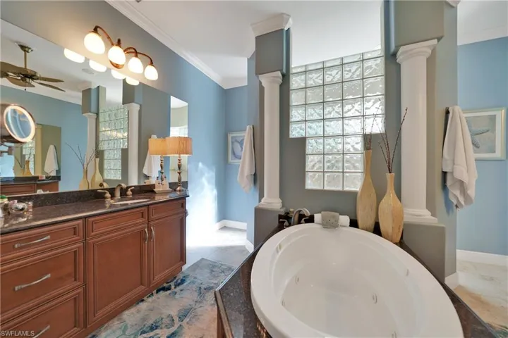 Bathroom with vanity, crown molding, ceiling fan, a tub to relax in, and decorative columns