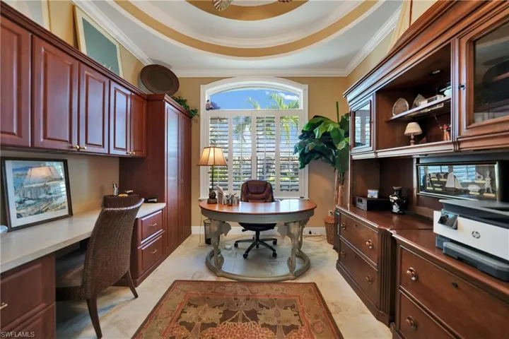 Home office with built in desk, a tray ceiling, ornamental molding, and light tile patterned flooring