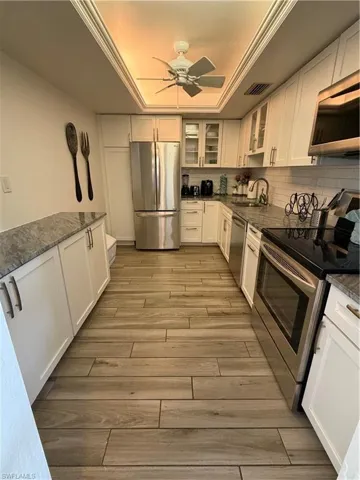 Kitchen featuring stainless steel appliances, white cabinets, glass insert cabinets, a raised ceiling, and ceiling fan