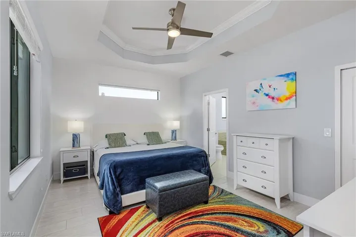 Bedroom featuring a tray ceiling, baseboards, visible vents, crown molding, and ensuite bath