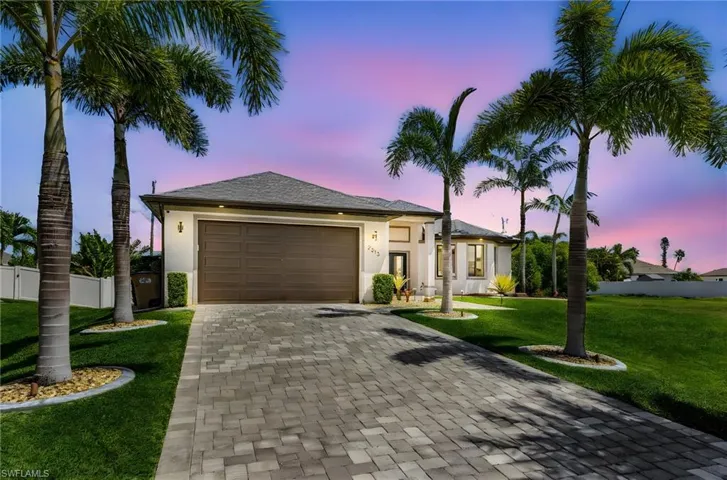 View of front facade featuring an attached garage, fence, stucco siding, and decorative driveway