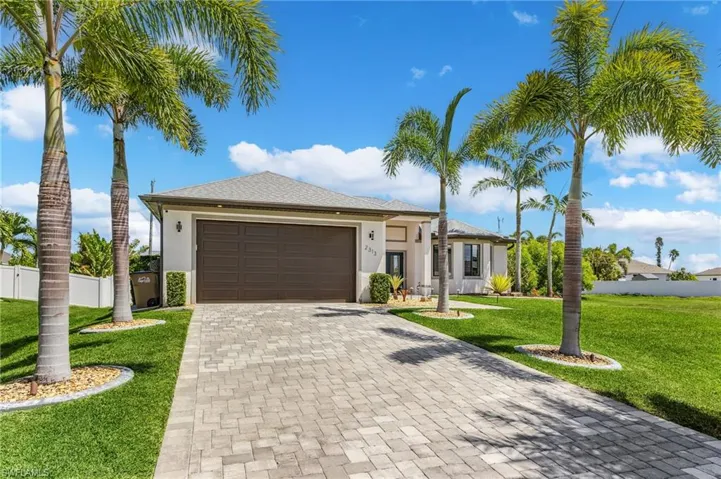 View of front facade featuring fence, stucco siding, an attached garage, decorative driveway, and a front yard