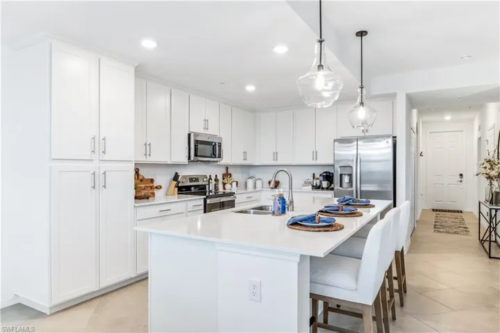 Kitchen featuring white cabinetry, stainless steel appliances, light tile patterned floors, and an island with sink