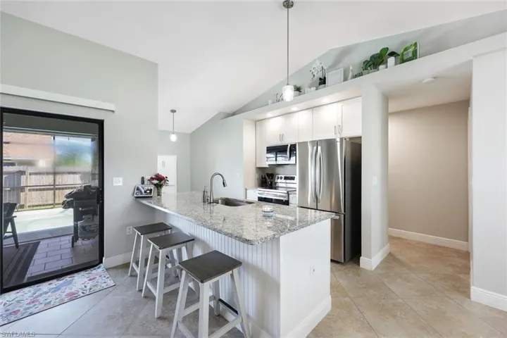 Kitchen featuring light stone countertops, appliances with stainless steel finishes, kitchen peninsula, sink, and vaulted ceiling