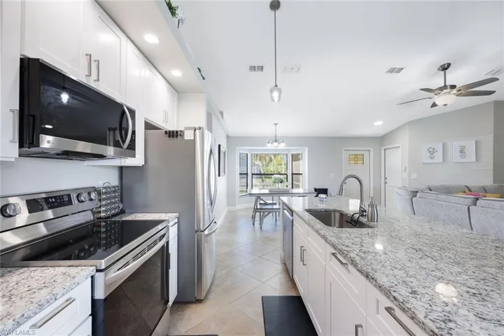 Kitchen featuring light tile floors, hanging light fixtures, sink, white cabinetry, and appliances with stainless steel finishes