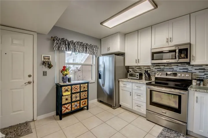 Kitchen featuring decorative backsplash, light tile patterned floors, white cabinets, baseboards, and appliances with stainless steel finishes