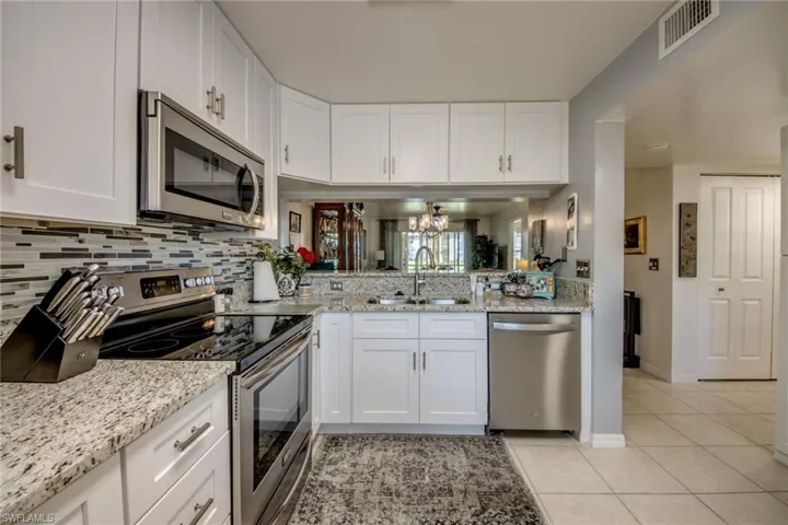 Well appointed kitchen with a double stainles steel sink, decorative backsplash, light tile patterned flooring, appliances with stainless steel finishes