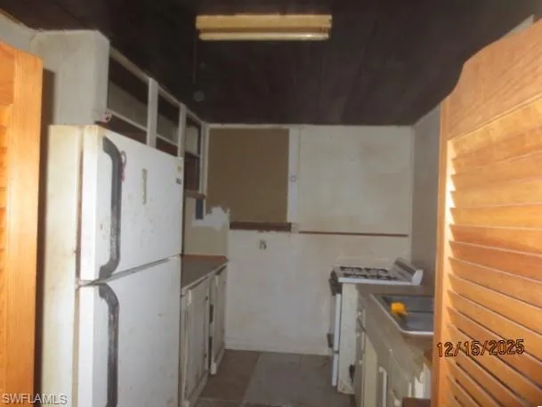 Kitchen with freestanding refrigerator, gas stove, dark tile patterned flooring, and light countertops
