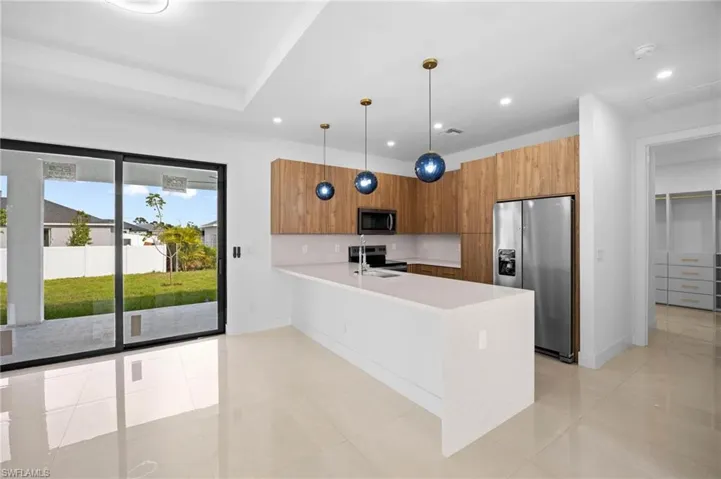 Kitchen with appliances with stainless steel finishes, modern cabinets, pendant lighting, a peninsula, and brown cabinets
